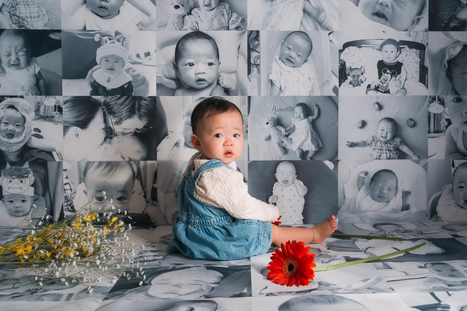 モノクロの思い出写真を一面に敷きつめた背景の真ん中に座る1歳の赤ちゃん