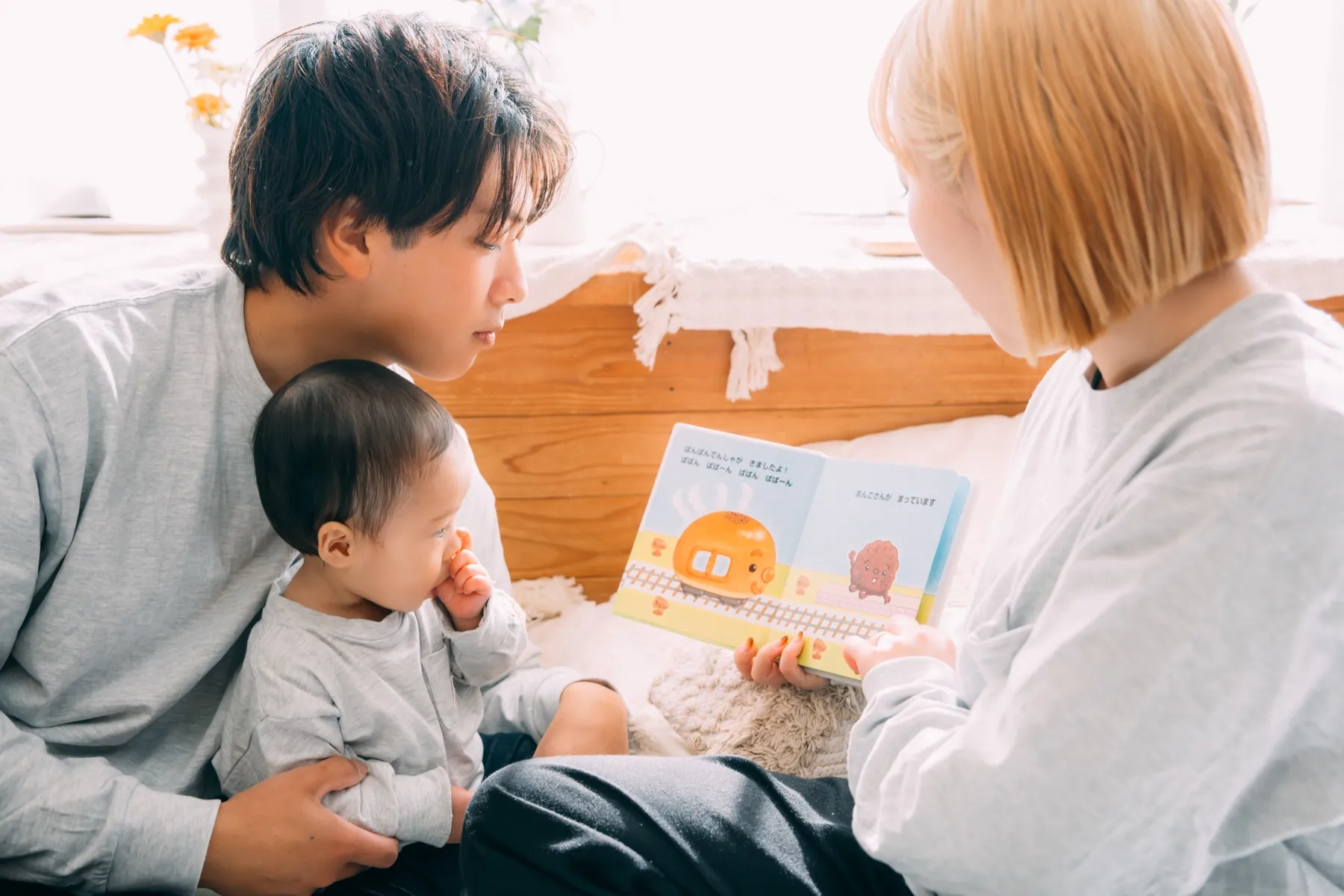 ご両親のあいだで絵本の読み聞かせを聞く赤ちゃん